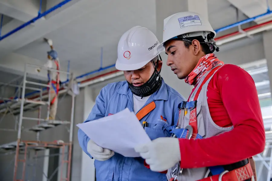 Two technicians in hard hats reviewing drawings on site